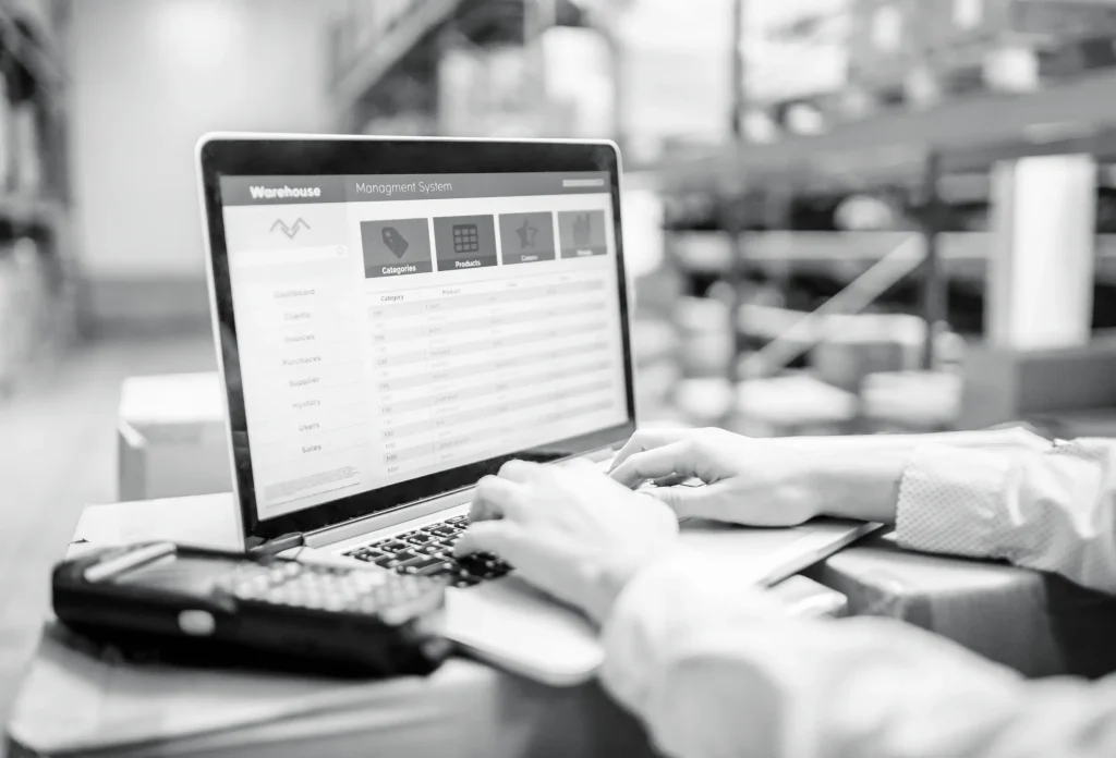 Hands typing on laptop while managing warehouse inventory and order system