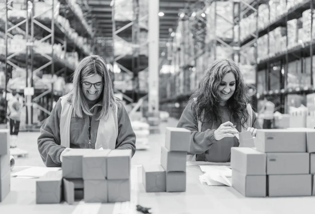 Two female warehouse workers sorting and packing small items at workstation