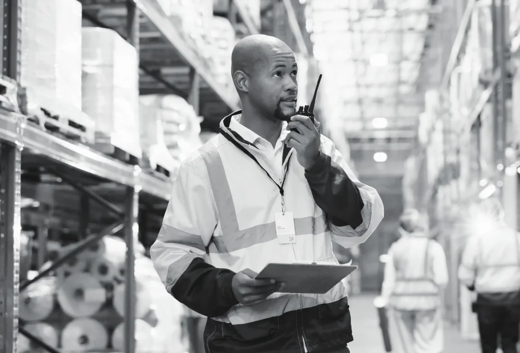Male warehouse worker in safety vest using two-way radio for communication