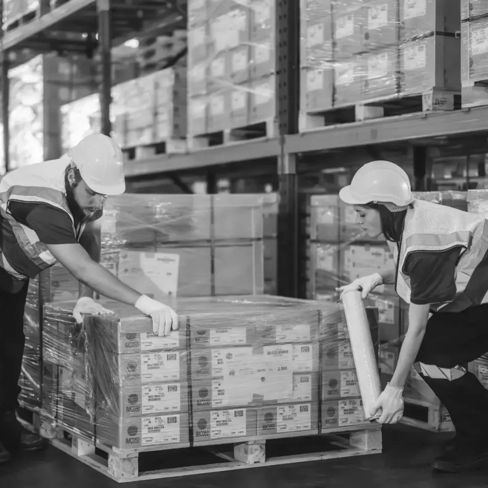 Warehouse workers in hard hats wrapping and preparing large pallet for shipping